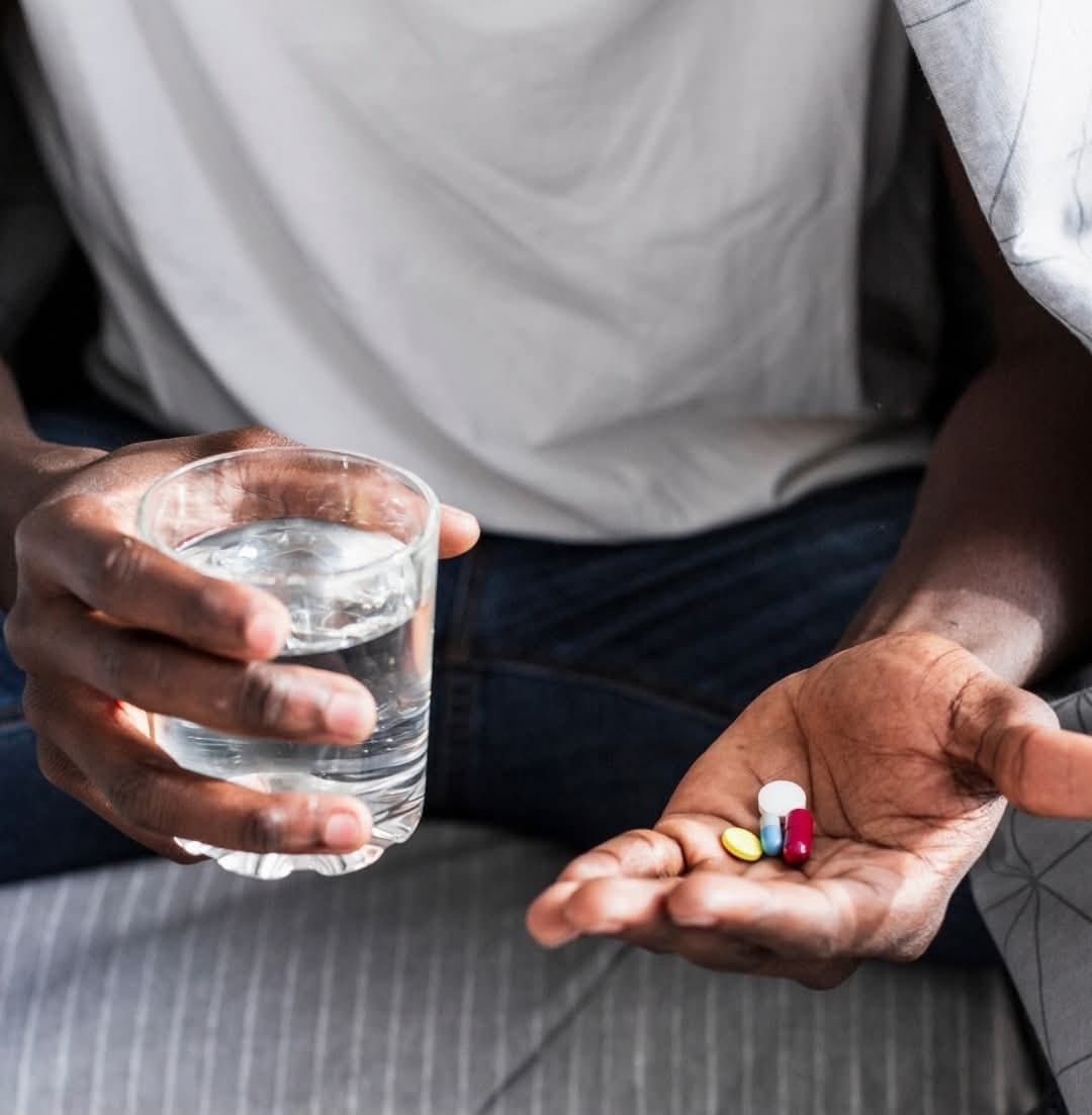 A person holding medication and a glass of water